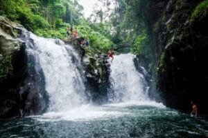 People cliff jumping Ubud at the stunning Aling Aling Waterfall in Bali, surrounded by lush greenery and cascading waters.