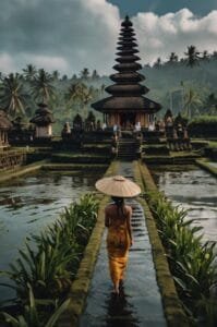 Beautiful Balinese temple surrounded by lush greenery and rice fields, showcasing the rich cultural heritage of Bali. A woman in traditional attire walks towards the temple, highlighting interesting facts about Bali, such as its spiritual traditions and stunning landscapes.