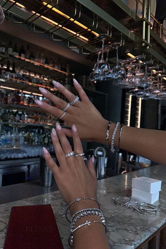 Hands adorned with sparkling sterling silver rings and bracelets displayed at an elegant bar setting, showcasing luxury jewellery perfect for those looking to buy silver in Bali.